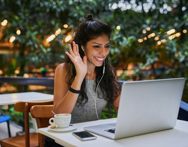 a student waves at a computer screen while sitting at a table